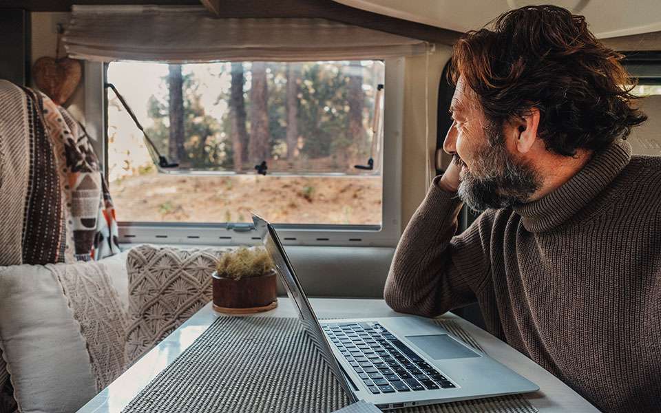 off grid job lifestyle with mature man working laptop inside camper van looking forest outside window van life people concept remote worker using online connection computer